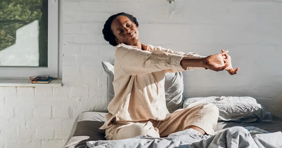 Person gently stretching arms overhead at a bright window during a morning break